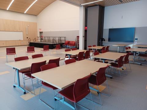 5 tables with chairs visible with an AV screen, large white board and a stage sitting off to the side